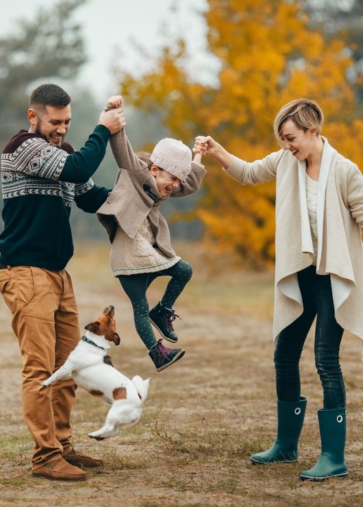 Rodzina bawi się z dzieckiem i psem na jesiennej polanie w otoczeniu kolorowych drzew