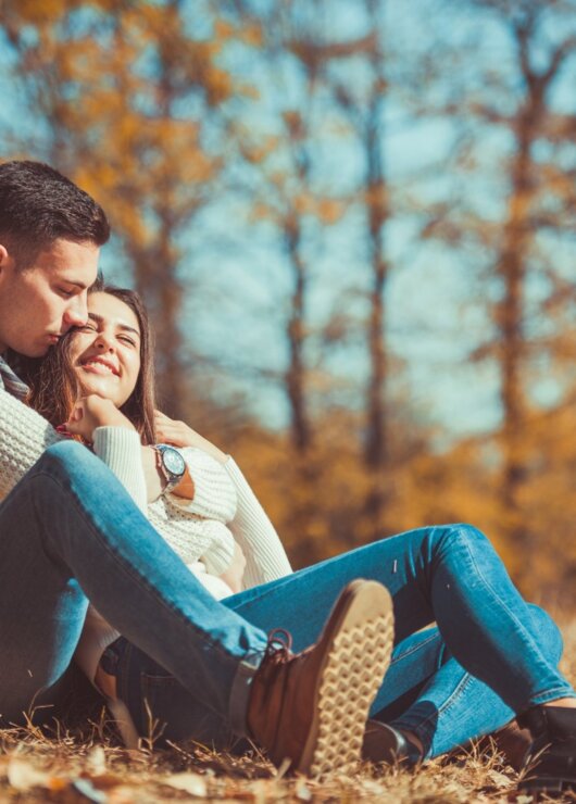 Para relaksująca się w jesiennym parku na kocu, otoczona złotymi liśćmi i ciepłym światłem