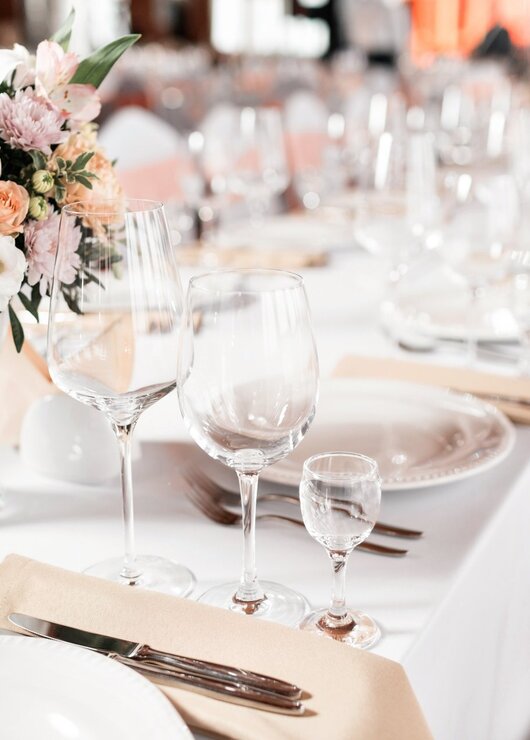 Elegantly set banquet table with white linen, glassware, and pastel floral centerpiece for a special event