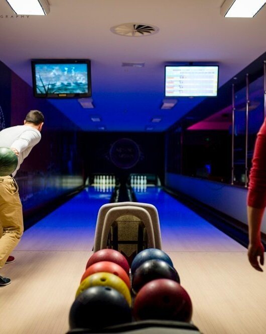 Goście grający w kręgle w nowoczesnej kręgielni hotelowej z kolorowymi kulami i telewizorami nad torami