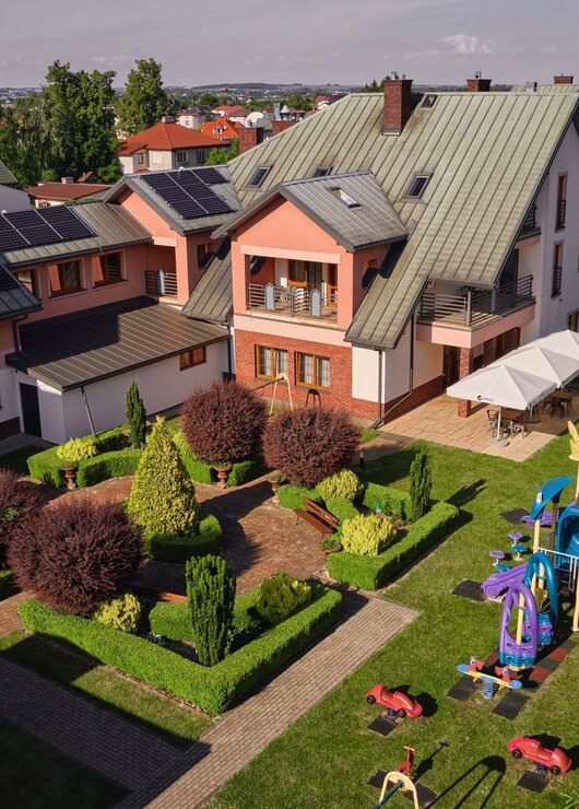 Kompleks hotelowy z nowoczesnym dachem, placem zabaw dla dzieci obok i zadaszonym tarasem na świeżym powietrzu.