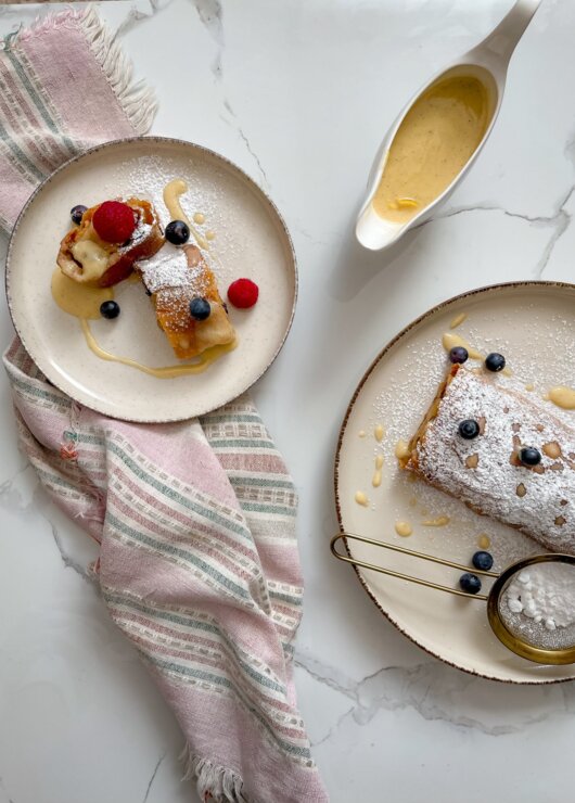 Deser naleśnikowy z owocami jagodowymi i malinami, posypany cukrem pudrem, z sosem waniliowym w wazie