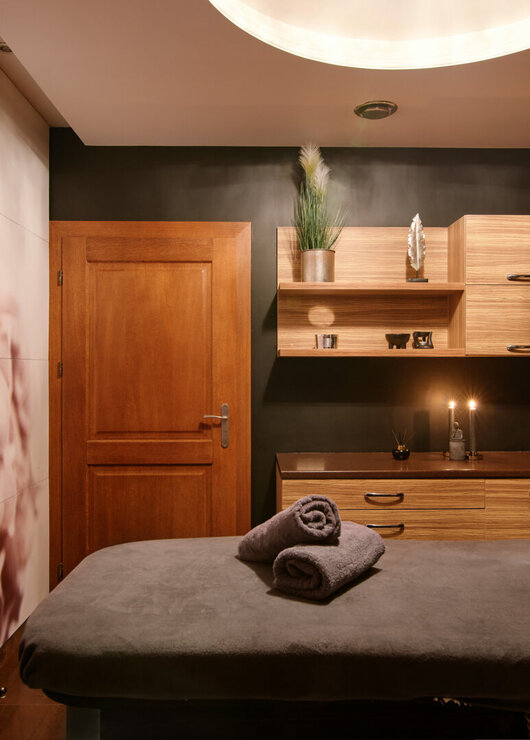 Cozy spa treatment room with wooden cabinetry, soft lighting, and rolled towels on a massage table for relaxation.