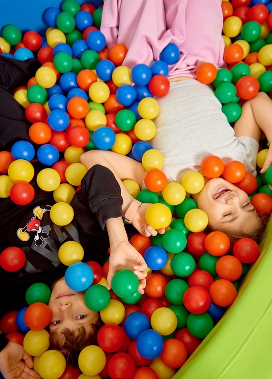 Two children laughing and playing in a colorful indoor ball pit, family-friendly play area at hotel or kids' club.