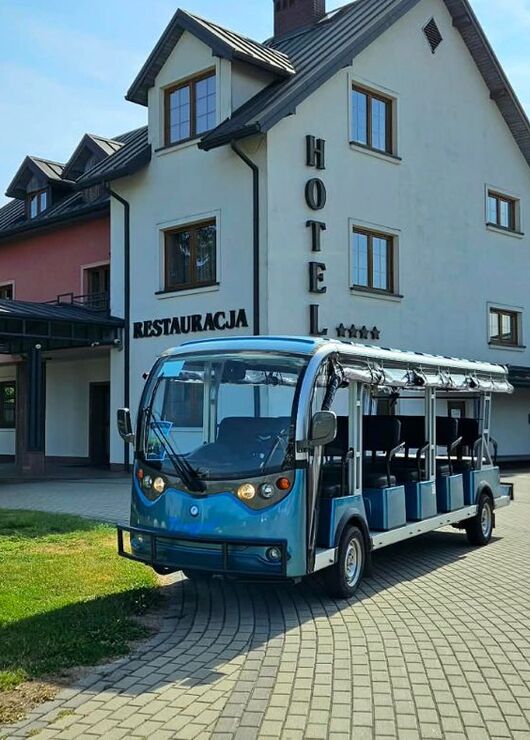 Open-air electric hotel shuttle parked by a multi-story hotel entrance with covered driveway, restaurant sign and spa building.