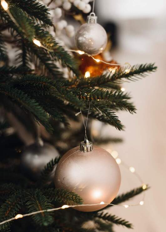 Green fir branches adorned with warm fairy lights and a matte rose-gold Christmas bauble, creating a cozy festive glow