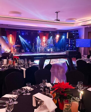Elegant banquet hall with stage lighting, round tables draped in black covers, set with glassware and silverware, ready for event