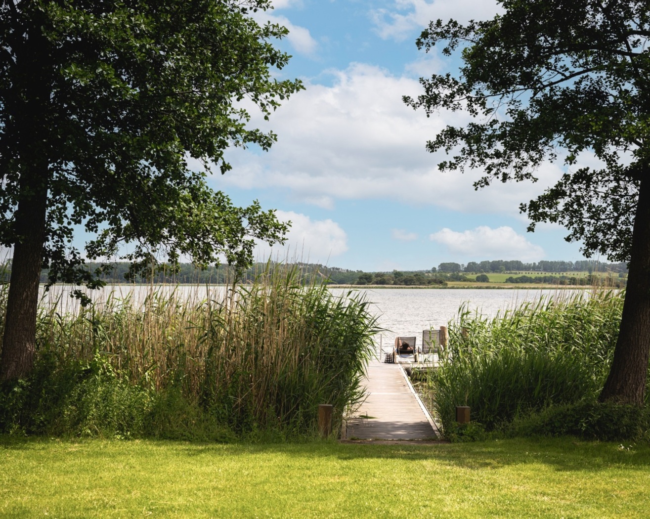 Die Liegewiese des Balmer See Resort mit dem Steg und den Liegestühlen mit Schild, Achterwasser