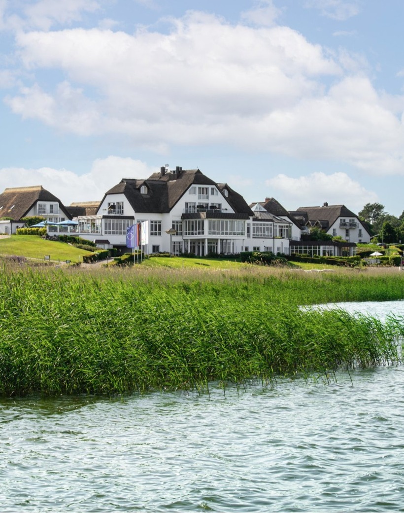 Thatched-roof lakeside hotel with white facades, waterfront terraces and balconies, manicured lawns and reed-lined shore