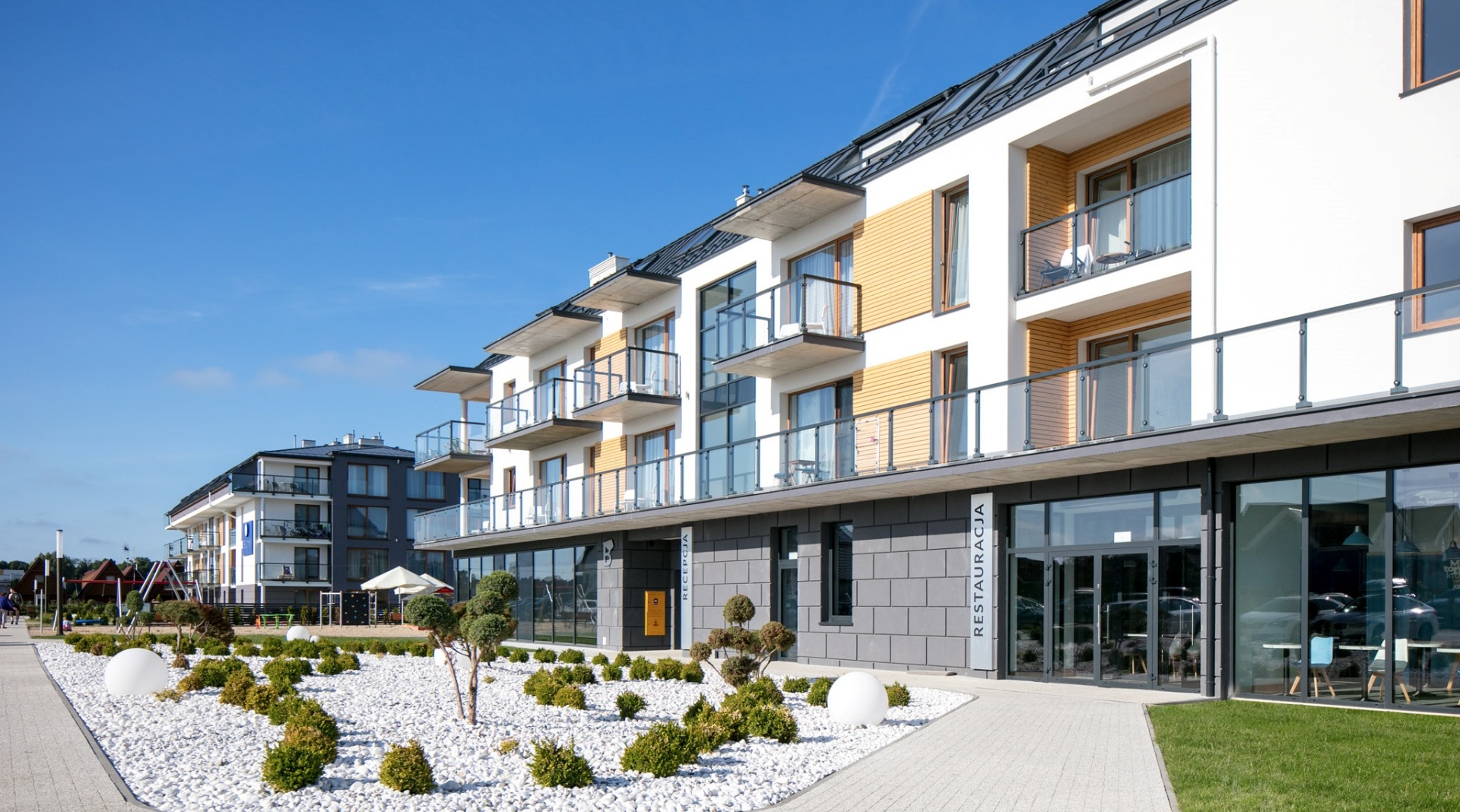 Nowoczesny hotel z balkonami, restauracją na parterze i zadbanym ogrodem z białymi kamieniami