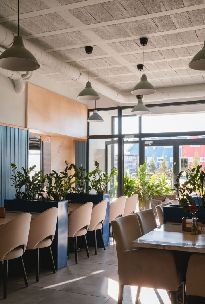 Jasna, nowoczesna jadalnia hotelowa z beżowymi krzesłami, dużymi oknami i licznymi zielonymi roślinami dla relaksującej atmosfery.