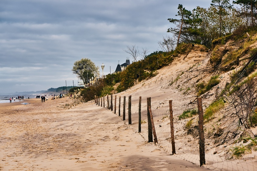 Sandstrand mit Holzzaun und Dünen, Gäste spazieren am Ufer bei bewölktem Himmel
