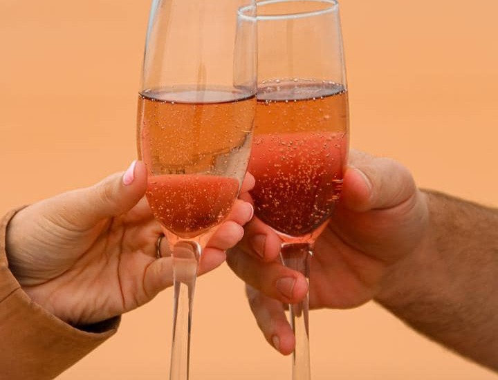 Two guests toasting with sparkling rosé in champagne flutes against a warm sandy backdrop, celebratory and intimate.