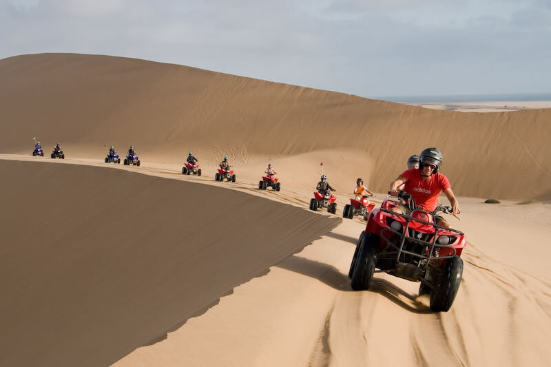 Guided ATV desert tour across sweeping sand dunes with helmets, thrilling off-road excursion and distant sea view