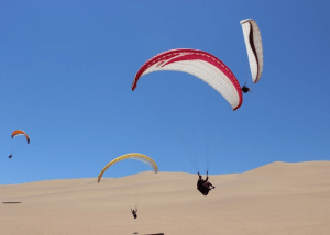 Paragliders soaring above golden sand dunes under a clear blue sky, ideal for a desert adventure experience