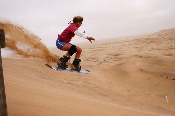 Guest sandboarding down a steep desert dune, kicking up sand on an adventurous outdoor excursion