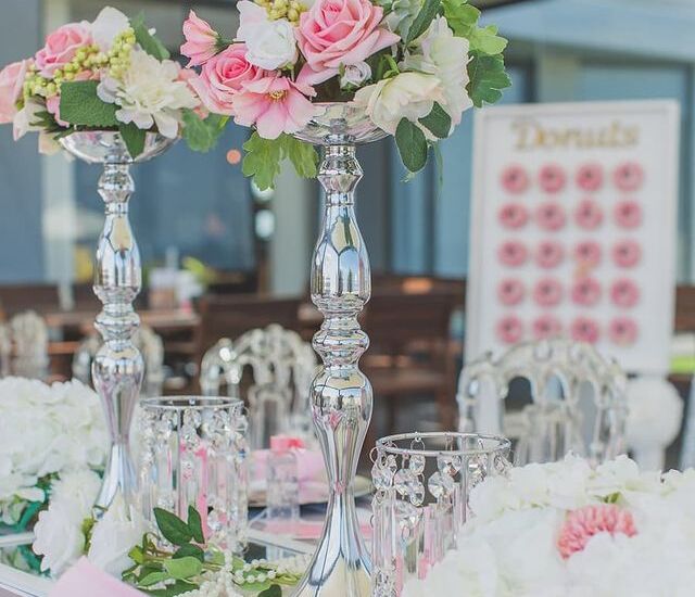 Elegant reception table with tall silver centerpieces topped with pink roses, crystal accents, pearl garlands and donut wall