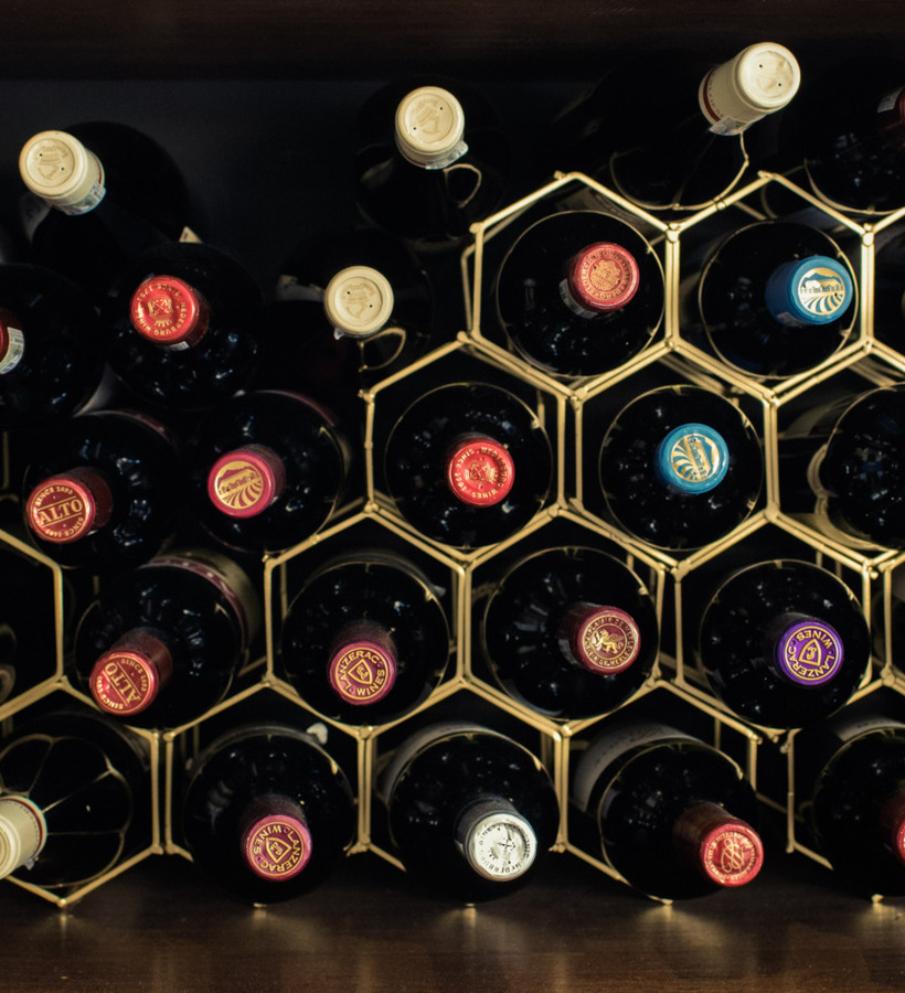 Stacked wine bottles in a honeycomb brass rack inside a wooden cabinet, assorted red and white labels for hotel bar.