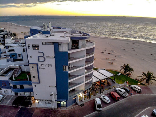 Beachfront resort with curved balconies and ocean-view terraces at sunset, poolside dining area and sandy beach beyond.