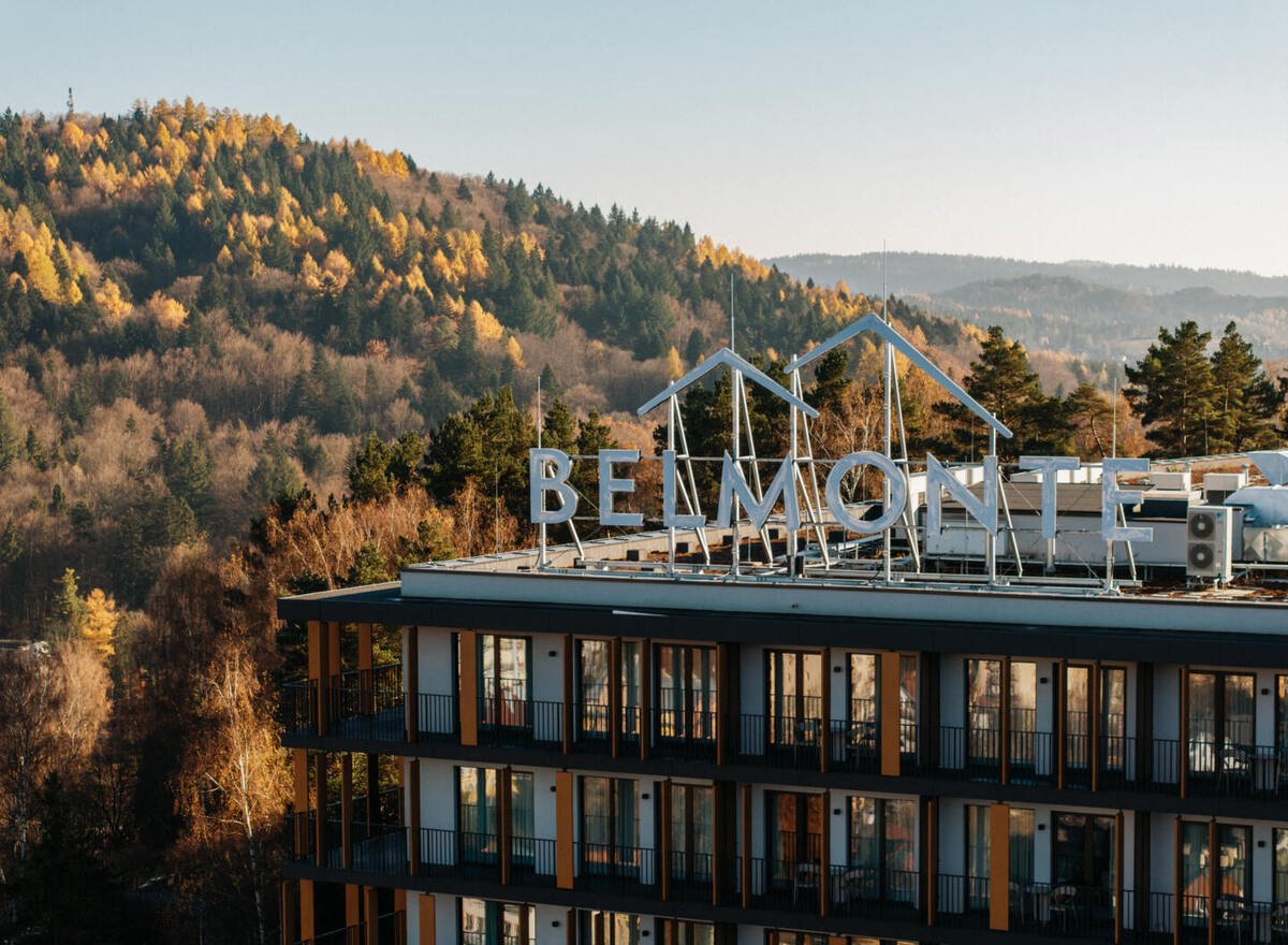 Modern hotel with balcony rooms and rooftop BELMONTE sign, overlooking golden autumn forested hills