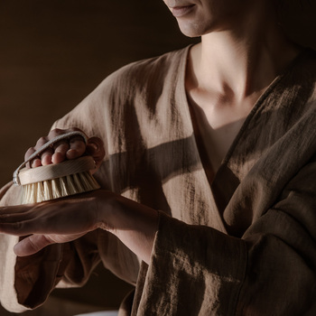 Gość w lnianym szlafroku używa naturalnej szczotki do masażu dłoni w ciepłym, przytulnym salonie spa