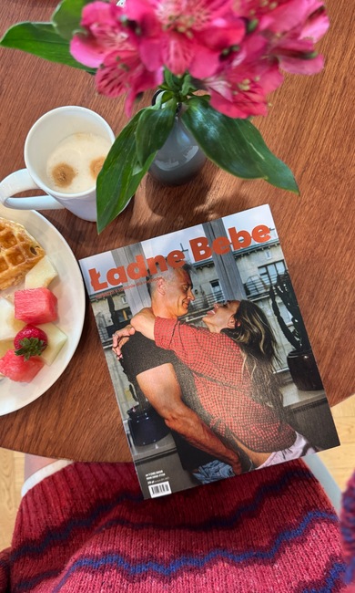 Śniadanie na drewnianym stole: gofr z owocami, cappuccino w białym kubku, różowe kwiaty w wazonie i magazyn lifestyle.