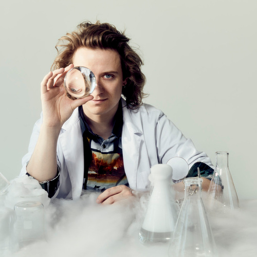 Mixologist in white coat holds a glass sphere to one eye amid beakers and swirling dry-ice vapor during a molecular cocktail demo