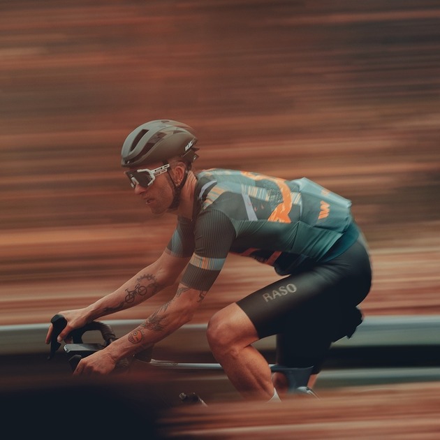Cyklista v aerodynamickom drese a prilbe preteká okolo, rozmazané pozadie zdôrazňuje rýchlosť a pohyb