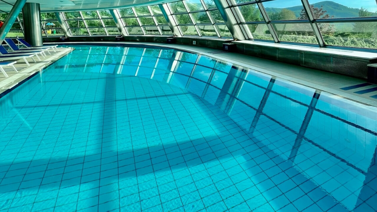 Ampia piscina coperta con grandi finestre che mostrano colline verdi e luce naturale.