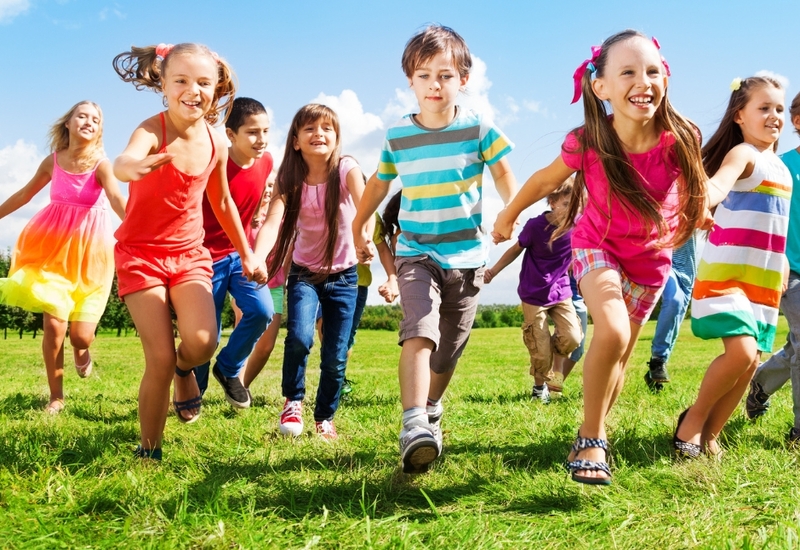 Mosolygó gyerekek csoportja fut és játszik egy zöld gyepűn, tiszta kék égbolt alatt.