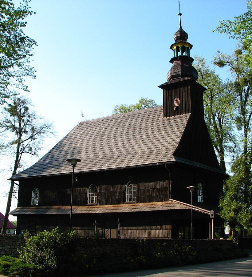 Chiesa tradizionale in legno con alta torre circondata da alberi verdi e muro di pietra sotto cielo sereno