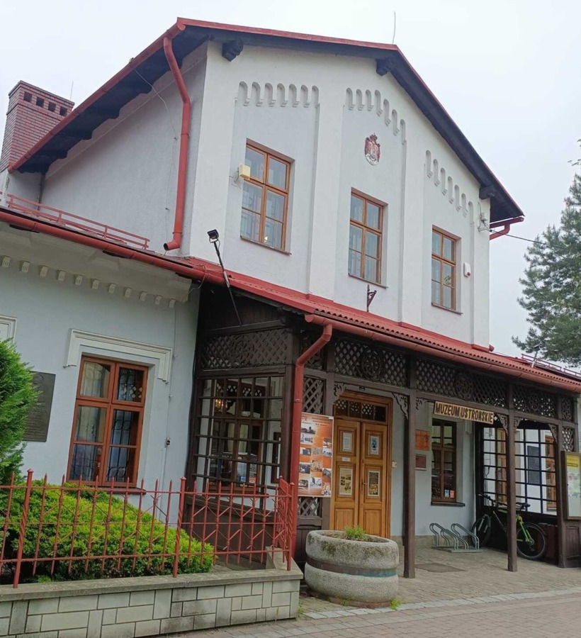 Edificio del museo di Ustroń con pareti bianche, camini in mattoni rossi e ingresso in legno con finestre decorative.