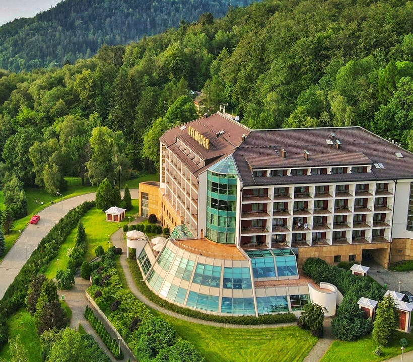 Hotel Belveder omgiven av skog, med modern glasarkitektur och balkonger med bergsutsikt.