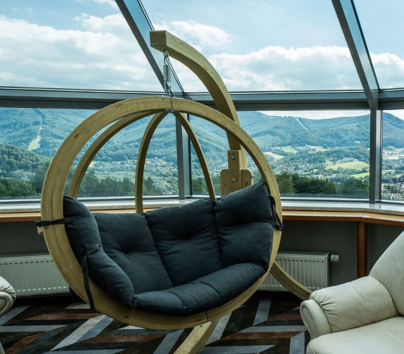 Rymligt lounge med trägunga, två crèmefärgade fåtöljer och panoramautsikt över gröna berg.