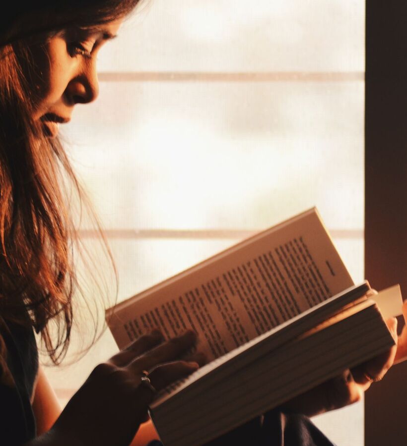 客人在温暖柔和的自然光中，舒适的酒店房间内阅读书籍，氛围宁静。