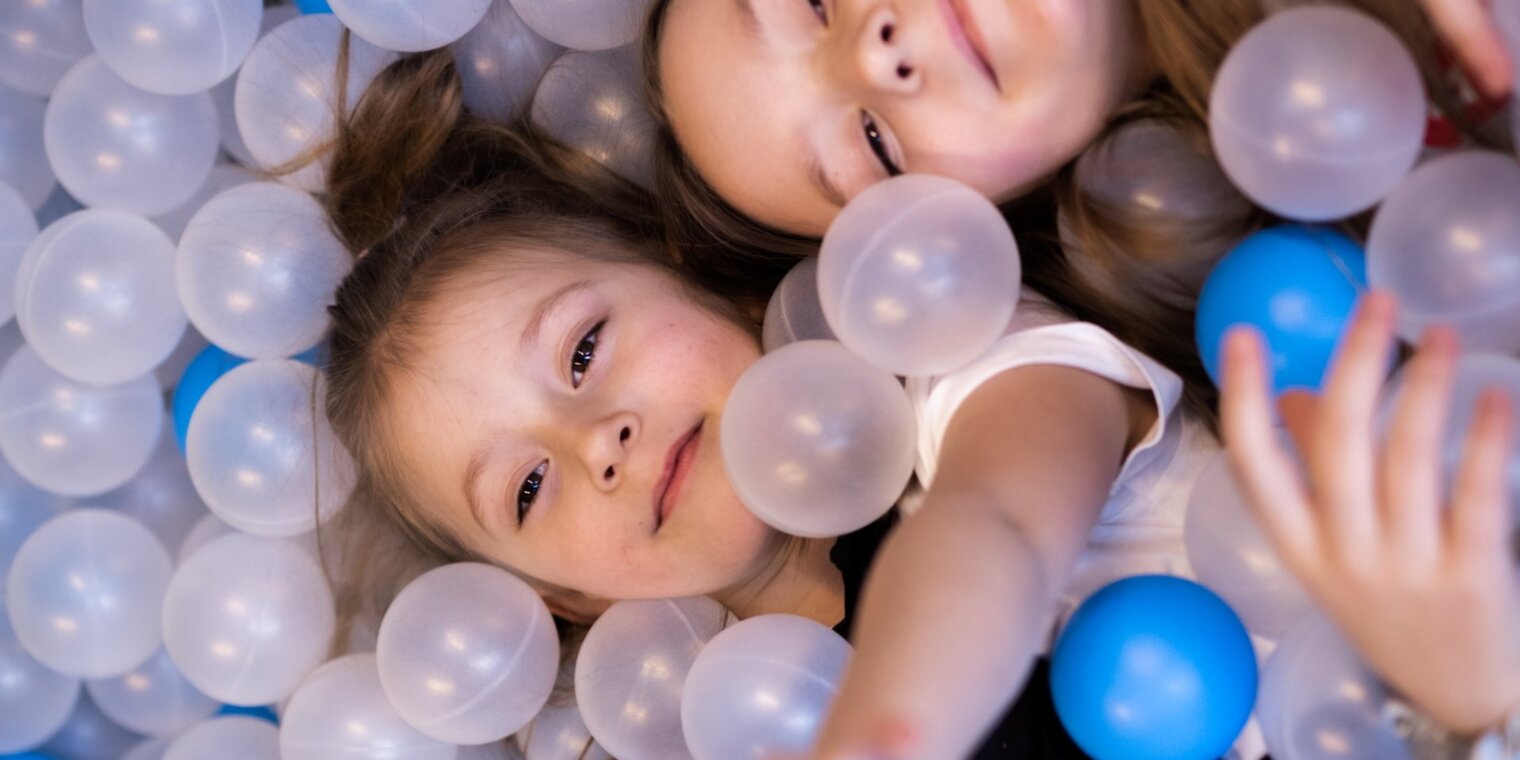 Two children playing in a ball pit with clear and blue balls in a hotel's family entertainment area.