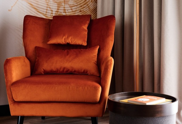 Cozy orange armchair with soft cushions next to a black side table holding books in a modern hotel room setting.