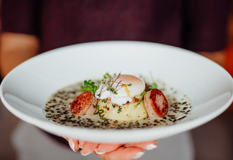 Delicate dish with poached egg, sausage, mashed potatoes, and herb sauce served on a white plate.