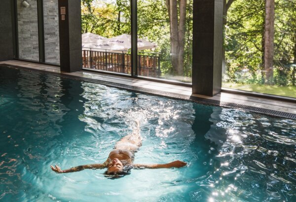 Relaxace v hotelovém vnitřním bazénu s velkými okny na zeleň a přirozené světlo.