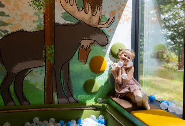 Child playing happily in a bright playroom with large window and colorful moose-themed wall decoration