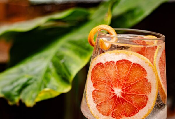 Osvěžující koktejl s plátkem grapefruitu a spirálou pomerančové kůry na pozadí zelených listů