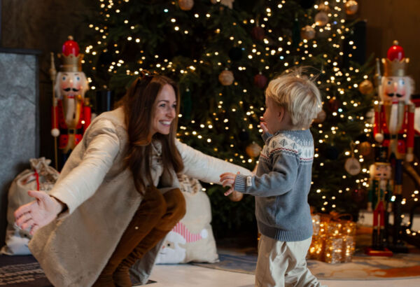 Mama z radością wita dziecko przy udekorowanej świątecznie choince w hotelowym lobby z nutcrackerami.