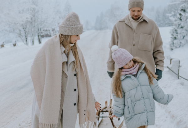 Family dressed in warm winter clothes walking on a snowy road in a scenic mountain winter landscape.