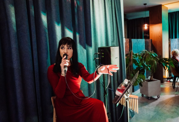 Woman in a red dress singing into a microphone in a cozy hotel lounge with dark curtains