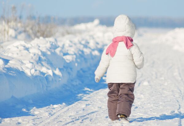Child in a white jacket and pink scarf walking along a snowy winter path in an open snowy landscape