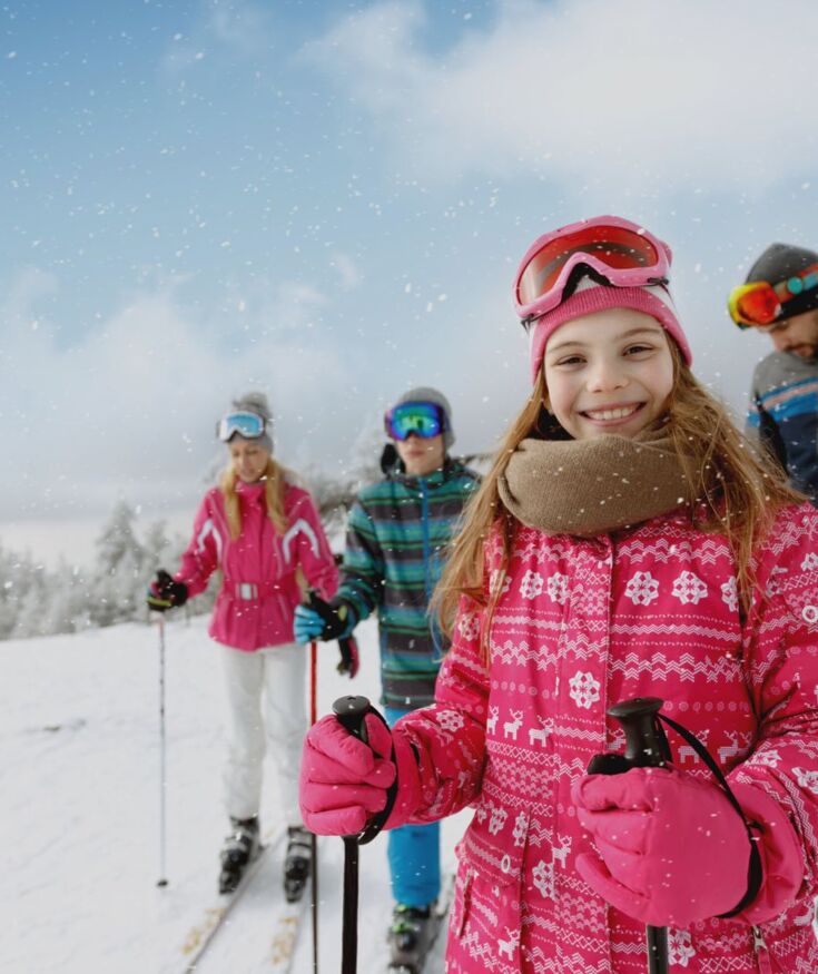 Familie genießt skifreudiges Wintererlebnis auf schneebedecktem Berghang mit klarem Himmel und verschneiten Bäumen.