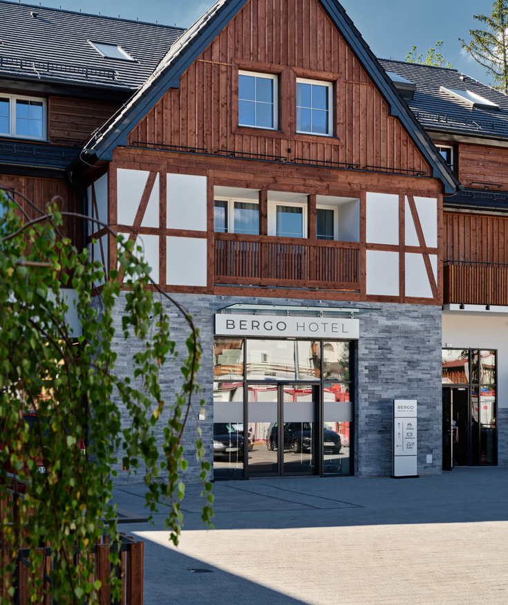 Entrance to Bergo Hotel featuring wooden facade, stone wall detail, and balcony above main doors.