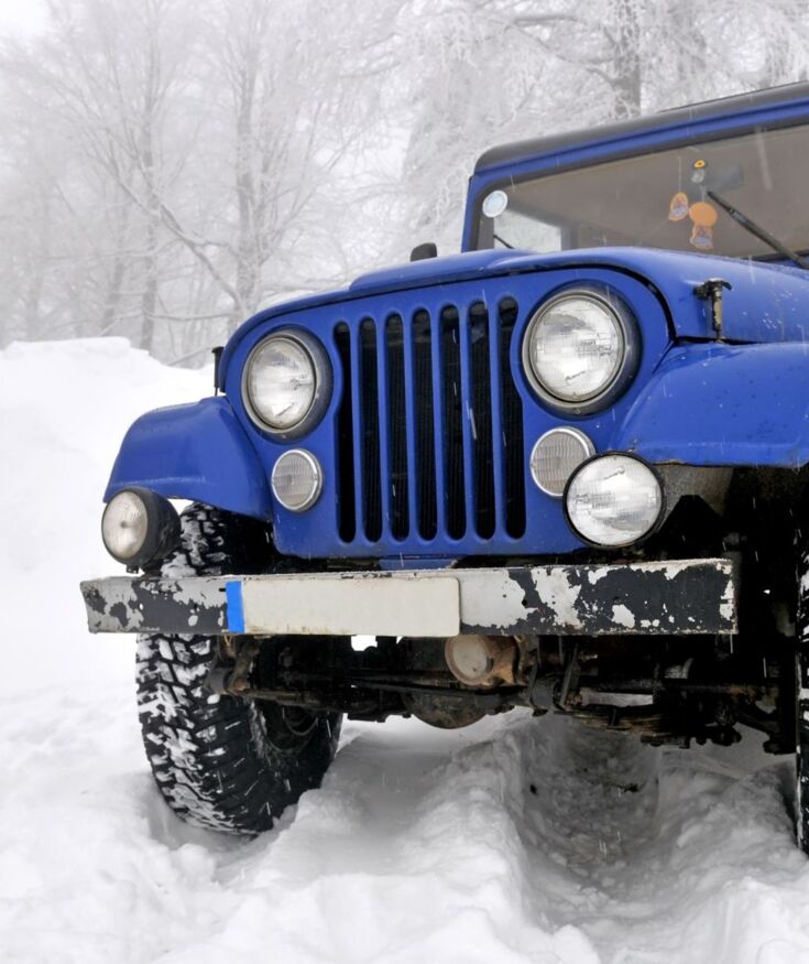 Modré terénní vozidlo zaparkované na zasněžené cestě obklopené sněhem pokrytými stromy v zimním horském lese