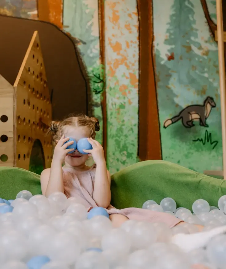 Child playing in a colorful hotel playroom with soft balls and forest mural, family-friendly indoor activity area