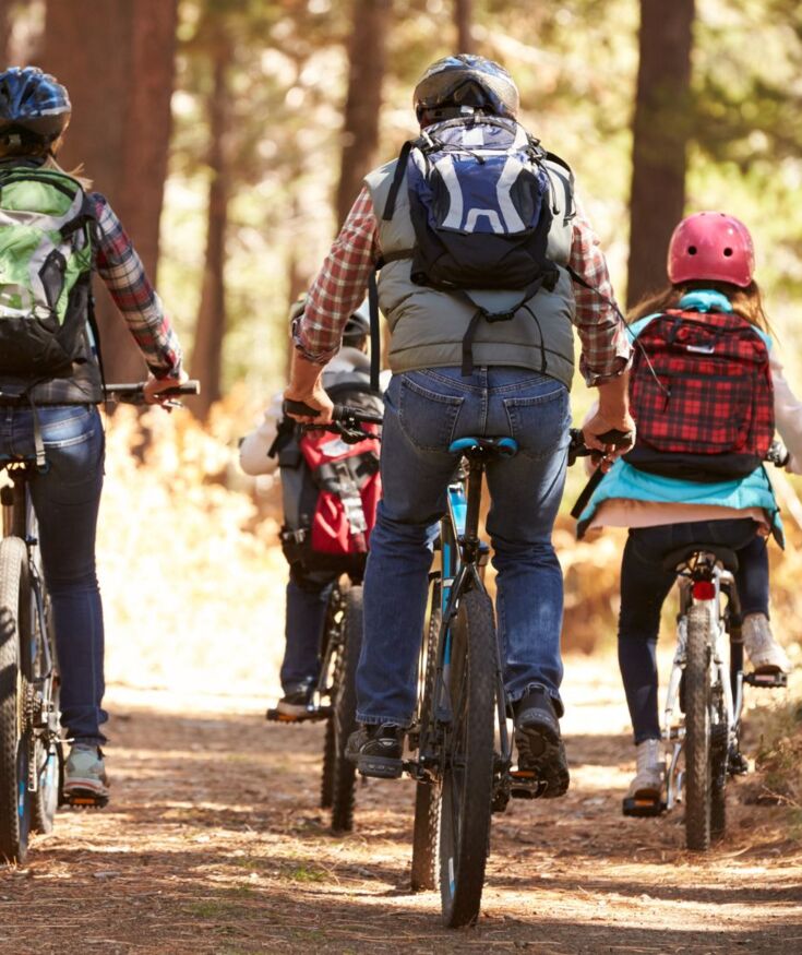 Family biking on a forest trail surrounded by autumn foliage and warm sunlight, enjoying outdoor adventure together.